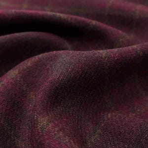 Puede incluir: Una tela de color burdeos profundo con un sutil patrón de cuadros en tonos oscuros. El material presenta una textura visiblemente ligeramente difusa con un tejido denso, mostrado en pliegues suaves y ondulados que crean sombras variables.