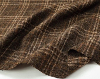 May include: A dark brown fabric featuring a textured, woven surface with a subtle plaid pattern in lighter tan and cream lines. The material is draped in soft folds, highlighting the thick, wool-like consistency and the intricate grid design.