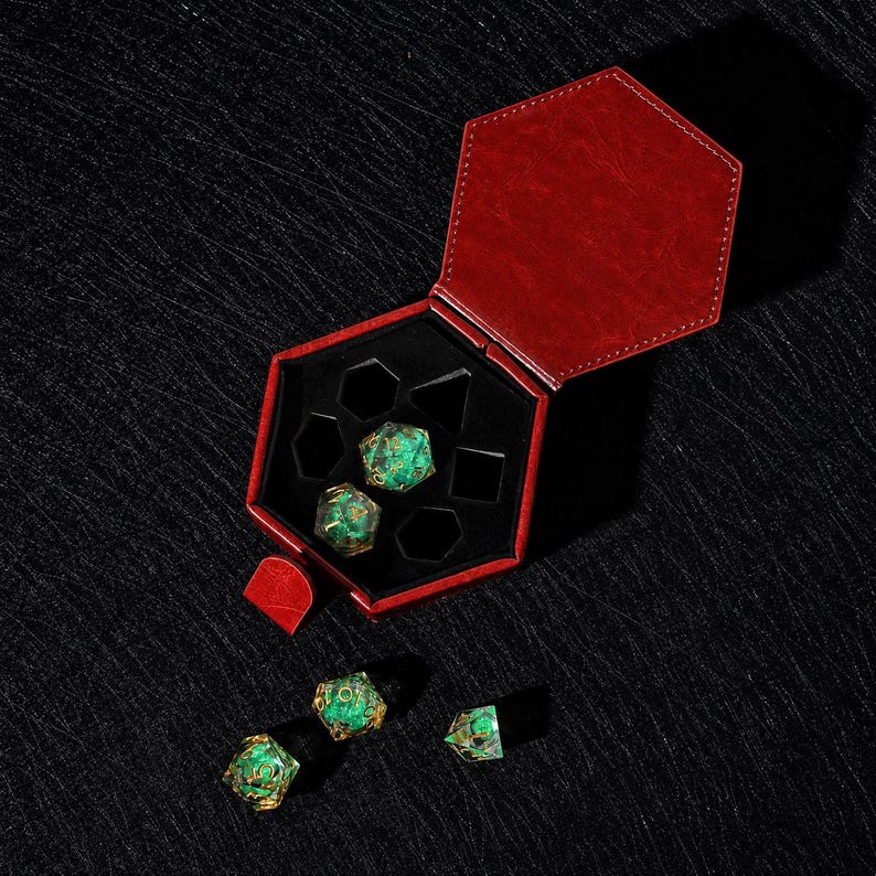 Peut inclure: Un &eacute;tui hexagonal en similicuir rouge avec un int&eacute;rieur en velours noir contenant deux d&eacute;s poly&eacute;driques vert translucide avec des chiffres dor&eacute;s, tandis que trois d&eacute;s verts assortis sont plac&eacute;s &agrave; l'ext&eacute;rieur du bo&icirc;tier ouvert.