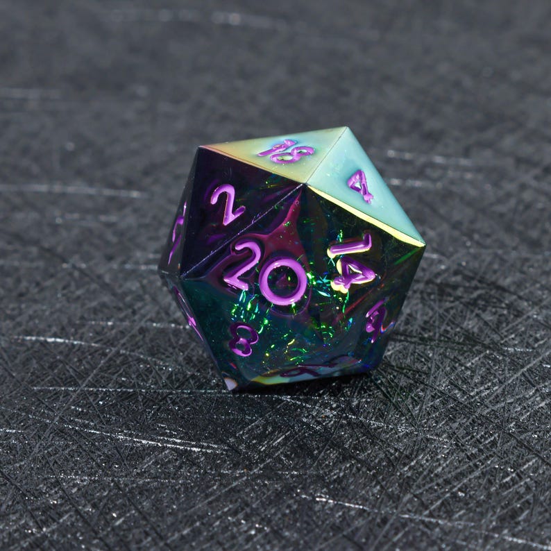 May include: A twenty-sided die featuring an iridescent, multi-colored metallic finish that shifts between shades of purple, green, and blue. The numbers are engraved into the surface and filled with a bright purple pigment for high visibility.