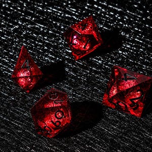 Peut inclure: Quatre d&eacute;s poly&eacute;driques rouge translucide avec des bords tranchants et des chiffres grav&eacute;s en noir. Les d&eacute;s pr&eacute;sentent une structure cristalline &agrave; facettes qui capte la lumi&egrave;re, affichant divers chiffres dont quatre et vingt.