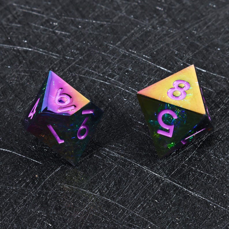May include: Two multi-faceted polyhedral dice featuring an iridescent, rainbow-colored metallic finish. The dice have sharp edges and deep purple engraved numbers, including a visible 6, 9, 5, and 8, with a dark, reflective, and textured surface.