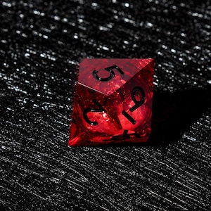 Peut inclure: Un d&eacute; poly&eacute;drique rouge translucide aux bords tranchants et aux chiffres grav&eacute;s en noir. Le d&eacute; pr&eacute;sente une surface &agrave; facettes qui capte la lumi&egrave;re, r&eacute;v&eacute;lant des textures internes et de la profondeur dans le mat&eacute;riau rouge, avec les chiffres 5, 2 et 9 visibles.