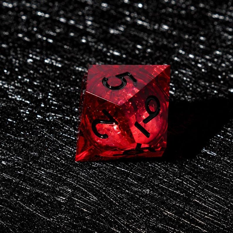 Peut inclure: Un d&eacute; poly&eacute;drique rouge translucide aux bords tranchants et aux chiffres grav&eacute;s en noir. Le d&eacute; pr&eacute;sente une surface &agrave; facettes qui capte la lumi&egrave;re, r&eacute;v&eacute;lant des textures internes et de la profondeur dans le mat&eacute;riau rouge, avec les chiffres 5, 2 et 9 visibles.