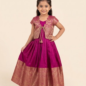 May include: A magenta floor-length dress with a pleated skirt and a wide gold metallic border at the hem. The dress features a matching short-sleeved jacket with a scalloped neckline, gold floral patterns, and a central tie closure with tassels.