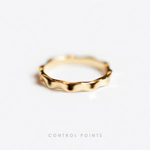 Könnte beinhalten: Ein goldfarbener Ring mit einem wellenförmigen, strukturierten Design. Der Ring besteht aus glänzendem Metall und befindet sich vor einem weißen Hintergrund. Der Text "CONTROL POINTS" befindet sich unten im Bild.