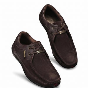 May include: A pair of dark brown suede and leather shoes featuring a moccasin-style toe, lace-up closure with metallic eyelets, and a small metallic brand plaque on the laces. The shoes have a low-top silhouette with a dark sole and red logo.