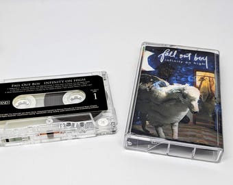 May include: A clear plastic cassette tape and its case for the Fall Out Boy album Infinity on High. The tape features a black label with white text listing tracks, while the case insert displays a blue night sky and a white sheep illustration.
