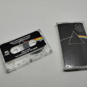 Può includere: Una musicassetta trasparente e la sua custodia con l'album "The Dark Side of the Moon" dei Pink Floyd. La cassetta ha un'etichetta nera con i titoli e un arcobaleno. La copertina dell'album è nera con un prisma e un arcobaleno.