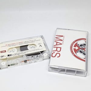 May include: A clear plastic cassette tape and its case for the album A Beautiful Lie by 30 Seconds to Mars. The tape label lists tracks including Attack and The Kill. The case insert features the band name in red and a circular skull graphic.
