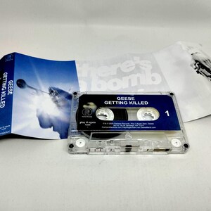 May include: A clear plastic cassette tape for the album Getting Killed by Geese, featuring a dark blue label with white text. The accompanying J-card insert displays a blue-toned image of a trumpet player and black and white text.
