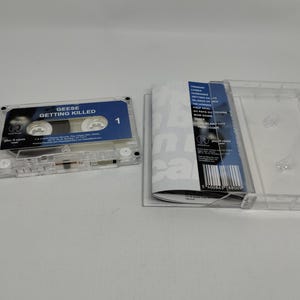 May include: A clear plastic cassette tape with a blue label reading Geese Getting Killed and a matching J-card insert featuring a tracklist including songs like Cobra and Bow Down, displayed next to an open transparent cassette case.