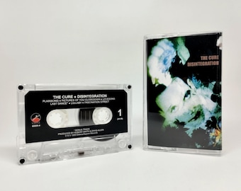 May include: A clear cassette tape and case featuring the album "Disintegration" by The Cure. The cassette tape has a black label with white text, including song titles. The album cover art features a dark image with blue and green hues.