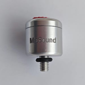 Puede incluir: Un dispositivo plateado con una parte superior roja y la palabra "MicSound" grabada en el lateral. Tiene una base roscada y una junta tórica negra. El dispositivo tiene forma cilíndrica.