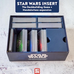 Peut inclure: Un insert de boîte de jeu bleu foncé pour Star Wars The Deckbuilding Game, doté de séparateurs internes pour organiser les cartes. L'avant de la boîte affiche le logo et le texte Star Wars. Plusieurs piles de cartes sont rangées à l'intérieur.