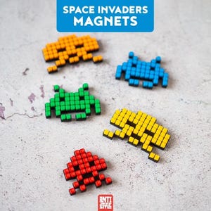 May include: Five pixelated Space Invaders magnets in orange, blue, green, yellow, and red. Each magnet features a grid-like design resembling classic arcade game characters. The text SPACE INVADERS MAGNETS appears at the top, and ANTI STYLE at the bottom.