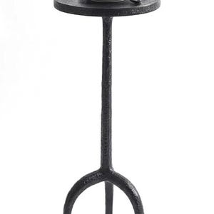 May include: A black, wrought-iron side table with a round top and three-legged base. A white coffee cup and saucer with a spoon rest on the table. The coffee has a decorative design on top.