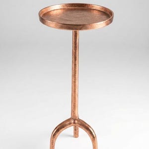 May include: A copper-coloured side table with a round top and a slender stem. The table has a three-legged base. The table is approximately 61 cm tall.