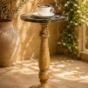 Peut inclure: Petite table ronde avec plateau en métal foncé et base en bois tourné. Une tasse à café blanche et une soucoupe avec une cuillère sont posées sur la table. La table mesure environ 71 cm de haut.