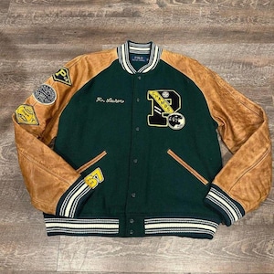 Puede incluir: Chaqueta universitaria verde y marrón con mangas de cuero. La chaqueta presenta parches, la palabra "CHAMPS" y la letra "P". La chaqueta tiene cuello, puños y dobladillo a rayas. La chaqueta tiene el texto "R. Lauren" bordado en la parte delantera.