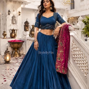 Puede incluir: Una mujer con un conjunto de dos piezas azul marino. La parte superior es una blusa corta con rayas doradas, y la falda es una falda amplia y fluida. Un chal magenta con bordados dorados está drapeado sobre una barandilla. El texto "StyleByVin" es visible.