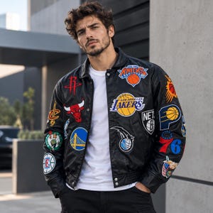 Op de afbeelding: Een zwart leren varsity-jack met talloze kleurrijke geborduurde NBA-teamlogo's en basketbalafbeeldingen op de voorzijde en mouwen, gedragen over een effen wit T-shirt met ronde hals. Het jack heeft een klassieke kraag en drukknopen.