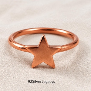 May include: A copper-toned metal ring featuring a prominent five-pointed star design centred on the band. The surface of the star and the circular band have a smooth, polished finish. The text 92SilverLegacys is printed below the ring.
