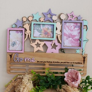 May include: Wooden trophy and photo display with three picture frames in pastel colours. The display features star and cheerleader cutouts, and the text "Go me". The display has a wooden shelf with slots for trophies.