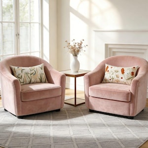 Peut inclure: Deux fauteuils assortis en velours rose poudré avec des dossiers arrondis et des assises profondes. Chaque fauteuil est doté d'un coussin rectangulaire à fond crème avec un imprimé botanique de fleurs sauvages dans des tons vert, jaune et orange.