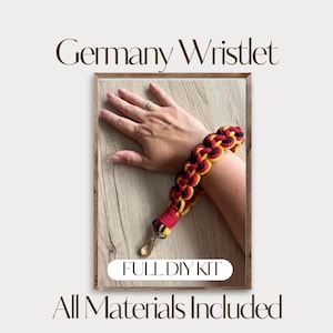Könnte beinhalten: Ein Armband mit einem geflochtenen Kordeldesign in Schwarz, Rot und Gelb, mit einem goldfarbenen Metallverschluss am Ende. Der Text Germany Wristlet, FULL DIY KIT und All Materials Included ist auf dem Bild zu sehen.
