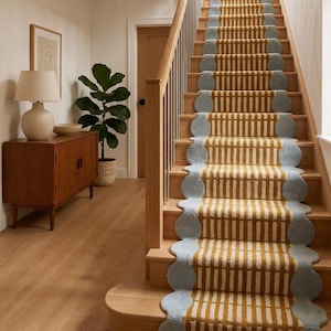 May include: A staircase with wooden steps and a runner rug. The rug has a yellow and white striped pattern with light blue scalloped edges. The wooden handrail has metal balusters. A wooden cabinet and a potted plant are visible.