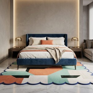 May include: A modern bedroom featuring a navy blue bed with a matching headboard, white bedding, and an orange accent pillow. A patterned rug with orange, teal, and white geometric shapes sits beneath the bed. Two gold lamps sit on wooden nightstands.