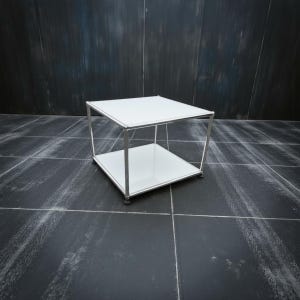 May include: A modern, square side table with a white top and a lower shelf. The table has a chrome-colored metal frame. The table is approximately 18 inches wide and 18 inches deep.
