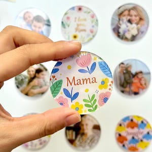 May include: A clear, round magnet with the word "Mama" in red script, surrounded by a floral design in pink, blue, yellow, and green. Other magnets with photos and text are visible.