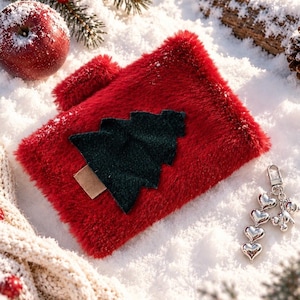 May include: A rectangular red faux fur pouch featuring a dark green fabric Christmas tree appliqué with a small brown trunk. A silver-toned metal keychain with four heart-shaped charms and a small bear figure is attached to the side of the pouch.