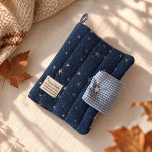 May include: A quilted navy blue fabric pouch featuring a pattern of small silver stars and dots. It includes a blue and white gingham check flap secured with a star-shaped button and a rectangular fabric label reading Natural Style.
