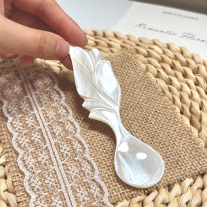 Könnte beinhalten: Eine weiße Keramik-Tasse mit schwarzem Henkel und dem Text "But First, Coffee" in schwarzer, handschriftlicher Schrift. Die Tasse steht auf einer weißen Oberfläche.