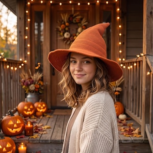 May include: A pointed orange knit hat with a wide brim, worn by a person with wavy brown hair. The hat features a textured, woven fabric construction with a distinct conical crown and a flexible, slightly downturned brim, providing a classic look.