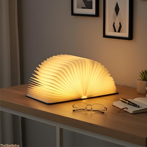 May include: A warm, glowing book-shaped lamp with open pages, emitting a soft light. The lamp sits on a wooden desk, next to a pair of glasses and a notebook. The lamp's design resembles an open book, creating a cozy ambiance.
