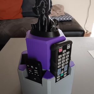 Może przedstawiać: Druk 3D organizer do pilota w kolorze szarym, fioletowym i czarnym. Organizer posiada czarną figurkę konia na górze. Baza posiada przegródki na piloty. Organizer stoi na stole.