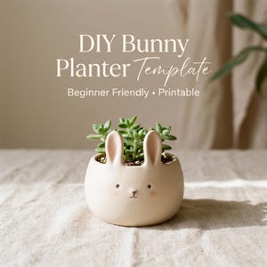 Op de afbeelding: Een beige keramische konijnenplanter met een vetplantje erin. De planter heeft konijnenoren en een geschilderd gezicht. Tekst op de afbeelding luidt "DIY Bunny Planter Template" en "Beginner Friendly • Printable".