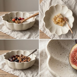 May include: Four off-white ceramic bowls and plates with a scalloped edge. The bowls contain cherries, walnuts, dried figs, and almonds. One plate holds honeycomb and a wooden honey dipper. The ceramic has a speckled finish.