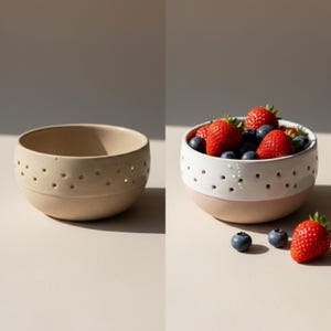 May include: Two ceramic bowls. One is beige with small, evenly spaced holes. The other is white with pink base and holes, filled with strawberries and blueberries. The bowls are on a neutral surface.