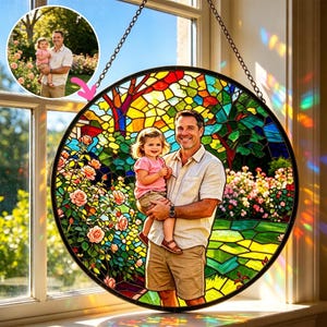 May include: A round stained glass window featuring a portrait of a father and child in a garden setting. The artwork is framed in black and hangs from a chain. The image within the glass is a vibrant mix of colors, including red, yellow, green, and blue.