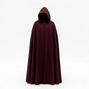 May include: A full-length, hooded cloak in a deep burgundy color. The cloak has a flowing design and a large hood. The fabric appears to be a soft, draping material. The cloak is displayed against a white background.