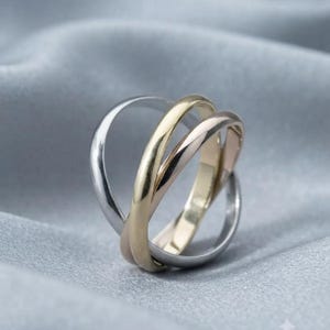 Può includere: Un anello intrecciato tricolore composto da tre fasce lisce e lucide nei toni dell'argento, dell'oro giallo e dell'oro rosa. Le tre distinte fasce metalliche sono intrecciate tra loro per formare un unico gioiello dal profilo arrotondato.