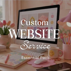 Op de afbeelding: Een computermonitor toont een website-ontwerpinterface met de tekst Custom WEBSITE Service Essential Pack. Op het bureau staan een roze lamp, een mok met een smiley, een notitieboek met bloemenpatronen en een vaas met roze tulpen.