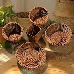 Puede incluir: Una colección de cestas marrones tejidas de varias formas y tamaños. El surtido incluye cestas redondas y cuadradas, todas hechas de materiales naturales. Las cestas están dispuestas sobre una superficie de madera, mostrando sus texturas y diseños.
