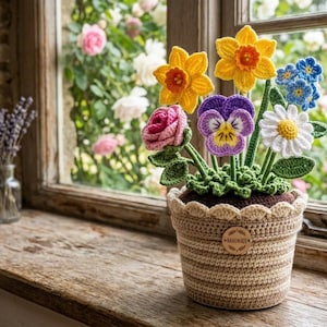 Puede incluir: Una maceta de flores hecha a mano con una variedad de flores coloridas, incluyendo narcisos, rosas y margaritas. La maceta es beige y está sobre un alféizar de madera. Un pequeño jarrón de cristal con lavanda está a la izquierda.