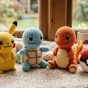 Peut inclure: Des personnages Pokémon crochetés, dont Pikachu, Carapuce et Salamèche, sont présentés sur une surface texturée. Un Poké Ball rouge et blanc et une tasse avec un motif Pokémon sont également visibles. Jouets faits à la main.